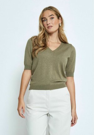Olivgrüner, kurzärmeliger Pullover mit V-Ausschnitt und geripptem Saum. Weicher Stoff, taillierte Passform. Kombiniert mit weißen, maßgeschneiderten Hosen.