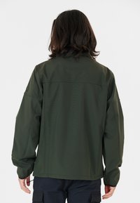 Veste softshell verte avec des manches longues, un col montant et une coupe droite, présentant des détails de couture subtils et des poignets élastiques.