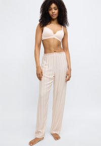 Reggiseno beige chiaro con texture liscia abbinato a pantaloni da pigiama larghi a righe in tessuto morbido con linee verticali in toni chiari.