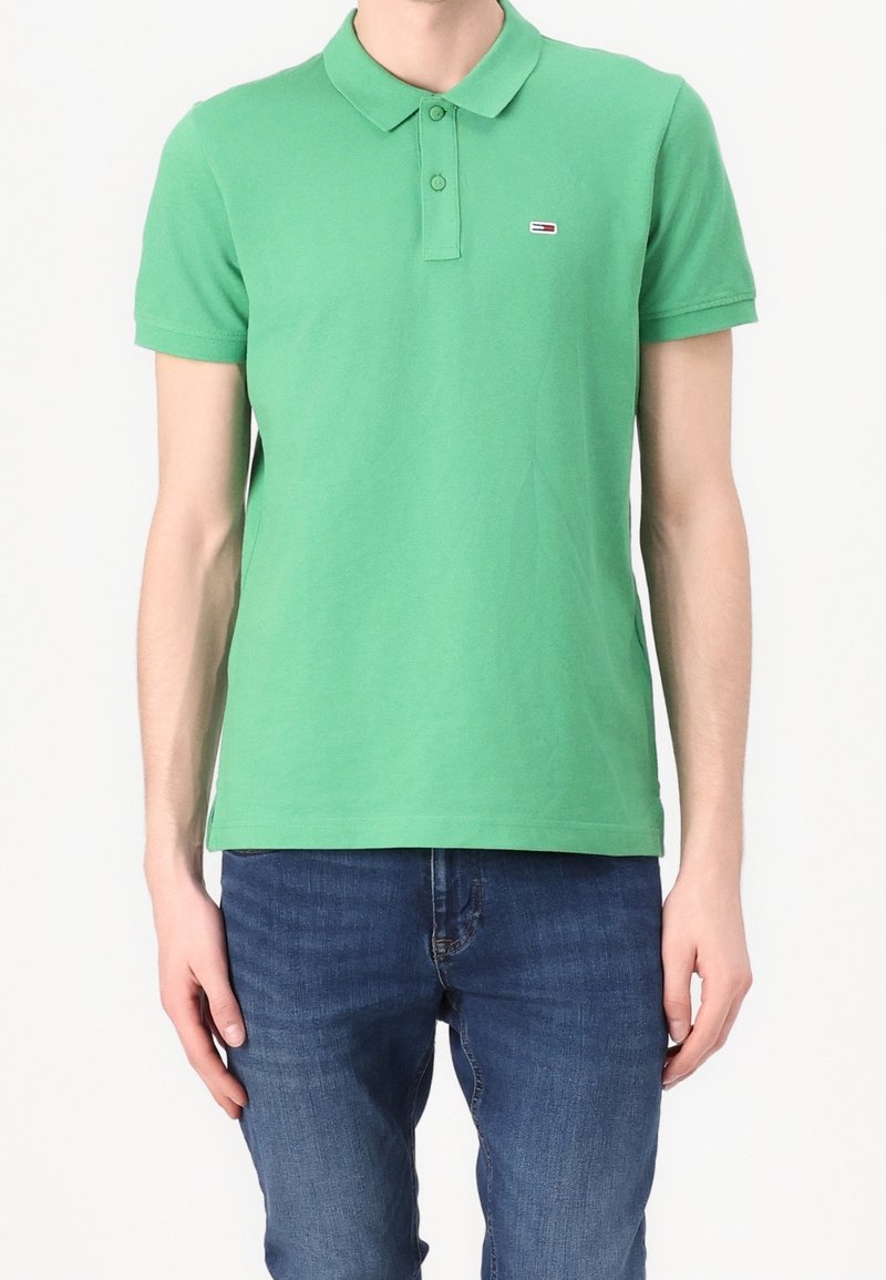 Green polo shirt made of cotton, featuring a collar, short sleeves, and a small logo on the chest. Paired with blue denim jeans.