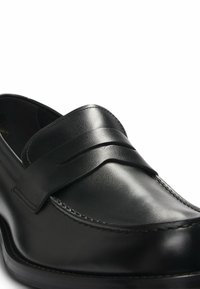 Black leather loafers featuring a stitched design and a wide strap across the vamp, with a smooth finish and rounded toe.
