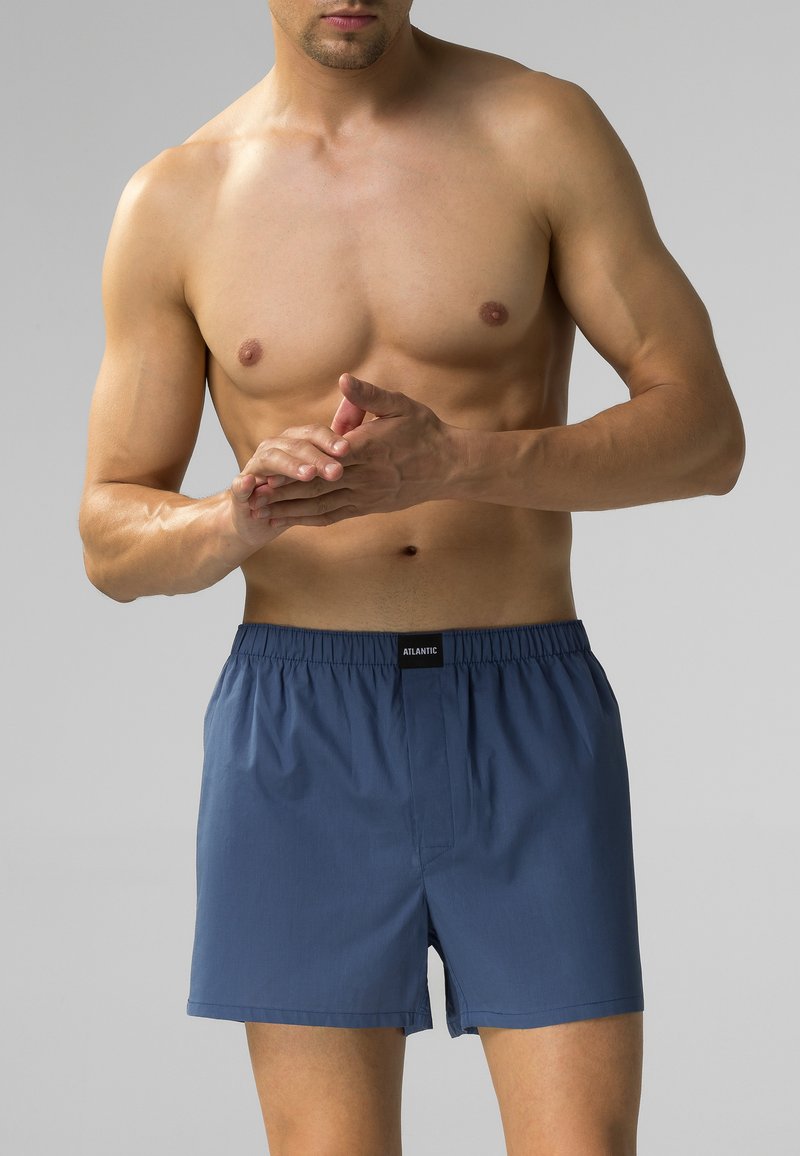 Ciemnoniebieskie kąpielówki z bawełny z elastycznym pasem, z przodem zapinanym na zamek i bez kieszeni, model pokazany z odkrytą górną częścią ciała.