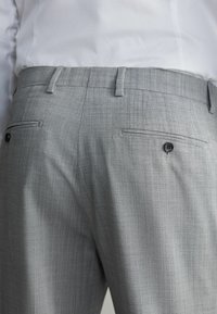 Pantalons tailleur gris en tissu texturé, dotés de deux poches arrière avec des boutons noirs et de passants de ceinture.