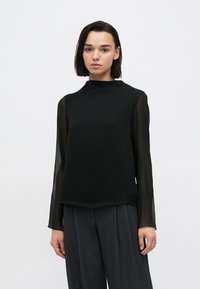 Μαύρο μακρυμάνικο τοπ με υψηλό λαιμό και διαφανή μανίκια, σετ με γκρι παντελόνια φαρδιάς γραμμής, με ομαλή υφή.