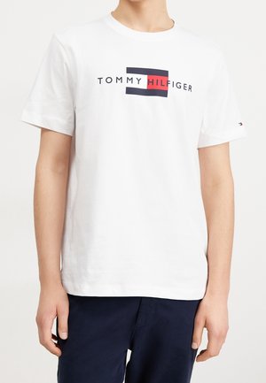 T-shirt en coton blanc avec un logo bleu marine et rouge centré sur la poitrine, col rond et manches courtes.