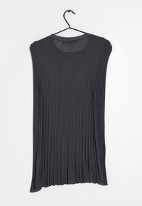 Haut à manches longues en tissu côtelé gris foncé avec un col arrondi et une texture. Suspendu à un crochet noir sur un fond blanc.