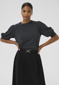 Tumehall toika lühikeste varrukatega blouse, millel on puhvvarrukad, koos kõrge talje musta seeliku ja kullatud nööbivöö detailiga.
