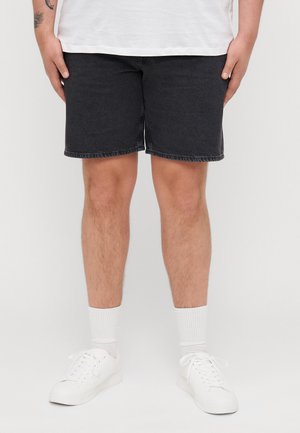 Svarte denimshorts har rett kutt og frynsete kant, kombinert med hvite sokker og hvite sneakers for et avslappet utseende.