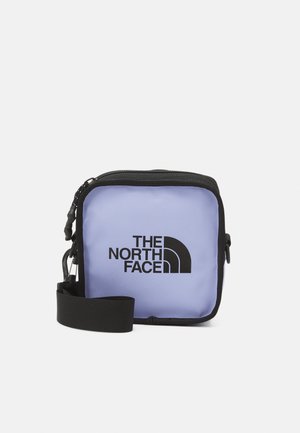 Kompaktowa kwadratowa torebka na ramię w kolorze lawendowym z czarną lamówką i regulowanym paskiem, na przedniej stronie z logo The North Face.