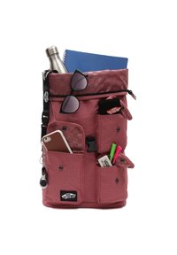 Un sac à dos rose avec un tissu texturé. Il comporte plusieurs poches, une bouteille d'eau, des lunettes de soleil et des articles de papeterie visibles.