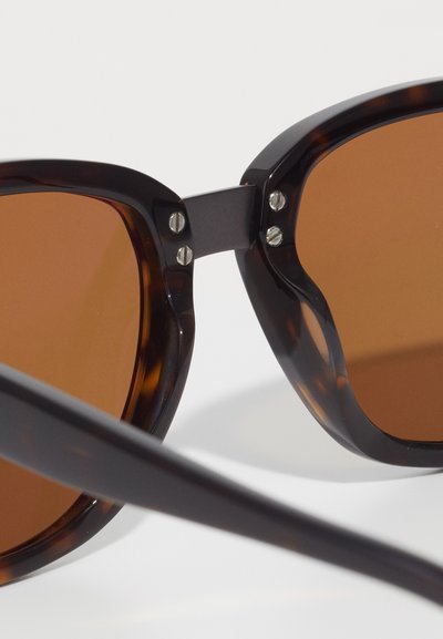 Brown-tinted sunglasses with a tortoiseshell frame, featuring angular design, metal accents at the hinge, and black temple arms.