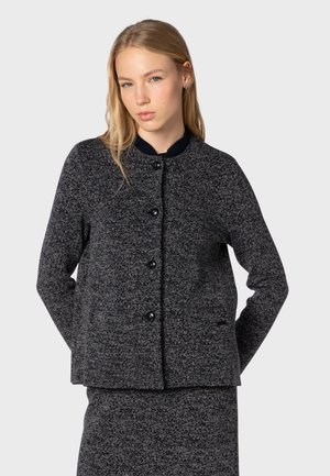 Dark textured jacket with a round collar, featuring black buttons and a subtle pattern. Worn with matching bottom garment.
