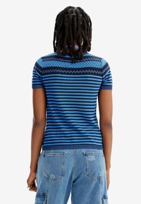 Suéter de manga corta a rayas azules que presenta un canesú texturizado y un diseño ajustado, combinado con unos vaqueros de un azul claro y detalles de costura visibles.