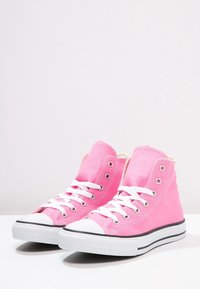 Růžové plátěné vysoké tenisky s bílými tkaničkami, gumovými špičkami a černými pruhovanými podrážkami. Obsahují kovové očky a texturovanou látku.