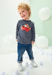 Marineblå langærmet skjorte med striber, dekoreret med et farverigt motiv af julemanden og gaver. Kombineret med opkørte jeans og hvide sneakers.