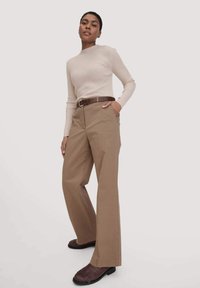 Beige geribbelde longsleeve top gecombineerd met een bruine wijde broek en een bruine riem. Schoenen zijn diepbruin met een gestructureerd franjes ontwerp.