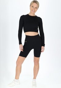 Sort ribbet cropped langærmet top sammen med højtaljede cykelshorts, der har metalknapdetaljer og en tætsiddende pasform.