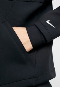 Zwarte sportieve sweatshirt met een hand in de zak. Het materiaal is glad met nauwsluitende boorden. Het Nike-logo is zichtbaar op de boord.