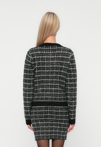 Cardigan à damier noir et blanc avec un ourlet et des poignets côtelés ; tissu en tweed texturé ; manches longues ; vue de dos.