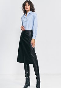 Jasnoniebieska, w poziome paski, koszula z długim rękawem, czarna skórzana spódnica midi oraz wysokie na kolana, czarne, buty o fakturze krokodylej. Gładkie tkaniny i dopasowany krój.