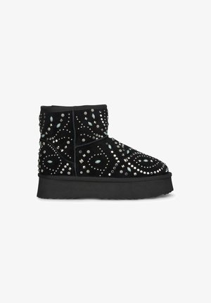 Black suede ankle boots with decorative studs and stones, featuring a patterned design and a thick, textured rubber sole.