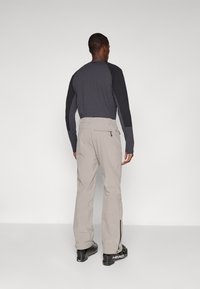 Light grey ski pants with zippered pockets and a straight leg design, paired with a long-sleeve dark top, viewed from the back.