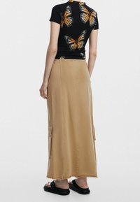 Top negro de manga corta con patrón de mariposas naranjas; falda maxi beige con bolsillos laterales; combinada con sandalias negras tipo slide.