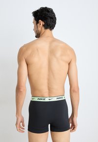 Schwarze Herrenslips mit einem hellgrünen Nike-Logo-Bund, die eine enge Passform und glatte Textur aufweisen, von hinten betrachtet.