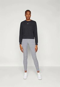 Černá mikina s kulatým výstřihem a malým logem, spojená se světlými šedými přiléhavými legínami s jemnou texturou a bílými teniskami.