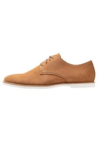 Chaussure en suède beige à lacets avec un bout rond, des détails de couture minimalistes et une semelle en caoutchouc blanche. Texture lisse avec un design classique.