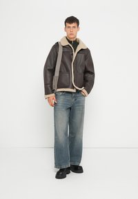 Bruine leren jas met schapenvacht kraag, twee voorzakken, knoopsluiting; gecombineerd met losse blauwe jeans en zwarte chunky schoenen.