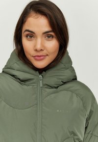 Olive green puffer jacket with a high collar, zip closure, quilted design, and logo on the chest. Smooth, insulated fabric texture.