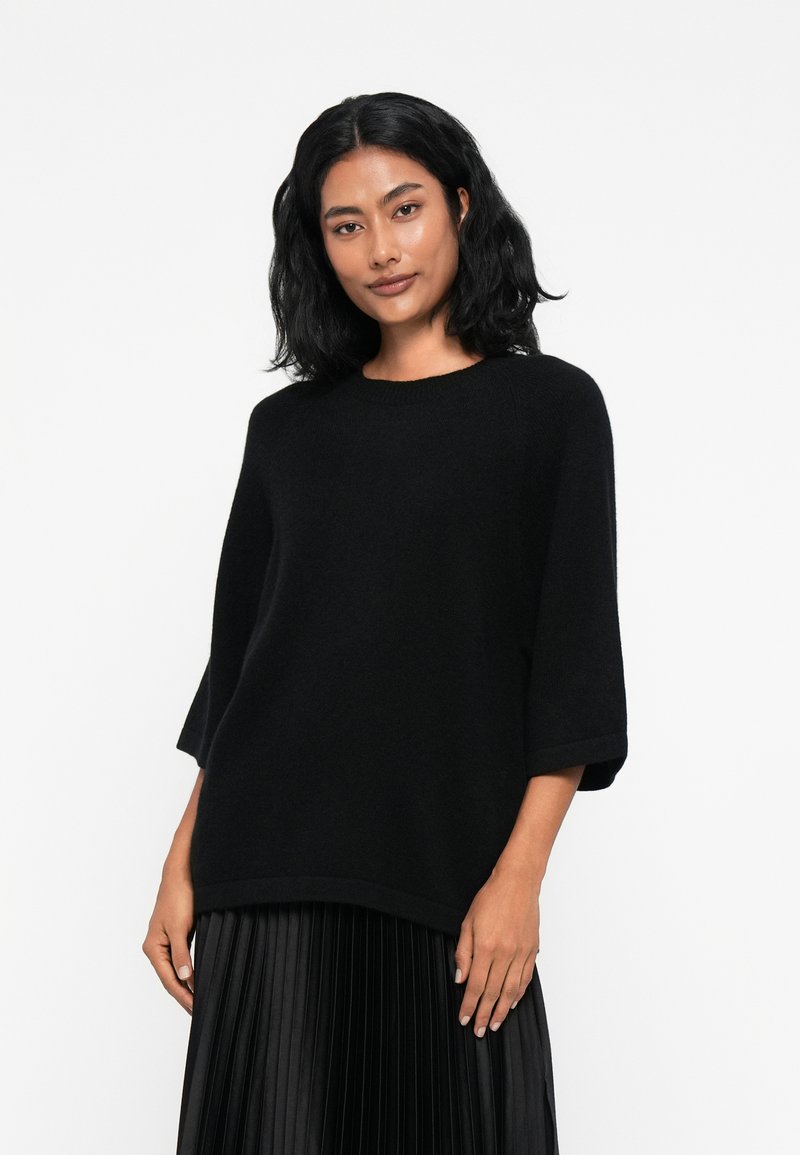 Pull noir oversize en tricot doux, avec un col rond et des manches trois-quarts. Texture lisse et coupe décontractée.