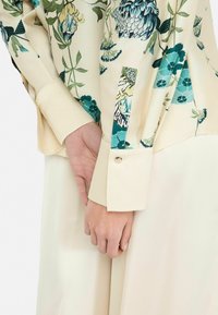 Bluse mit floralem Muster in Creme- und Türkistönen, mit langen Ärmeln, Knopfmanschette und seidiger Textur. Schlichter Schnitt und Designdetails.