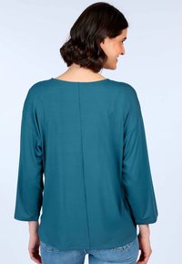 Tee in Türkis mit langen Ärmeln und rundem Ausschnitt, featuring einer Naht im Rücken. Weicher Stoff mit lockerer Passform und leicht gewelltem Saum.