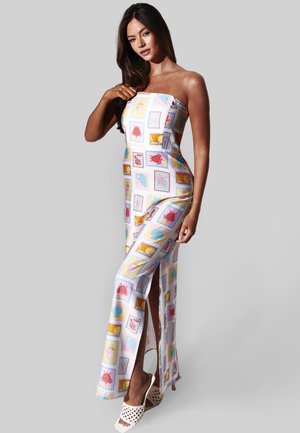 Vrouw draagt een strapless jurk tot op de grond met levendige patronen van schelpen en zeedieren, poseert tegen een effen lichte achtergrond.