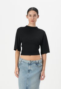 Zwarte cropped top met korte mouwen en een hoge halslijn. Gepaarde met een lichtblauwe denim rok met een split aan de voorkant en knoopsluiting.