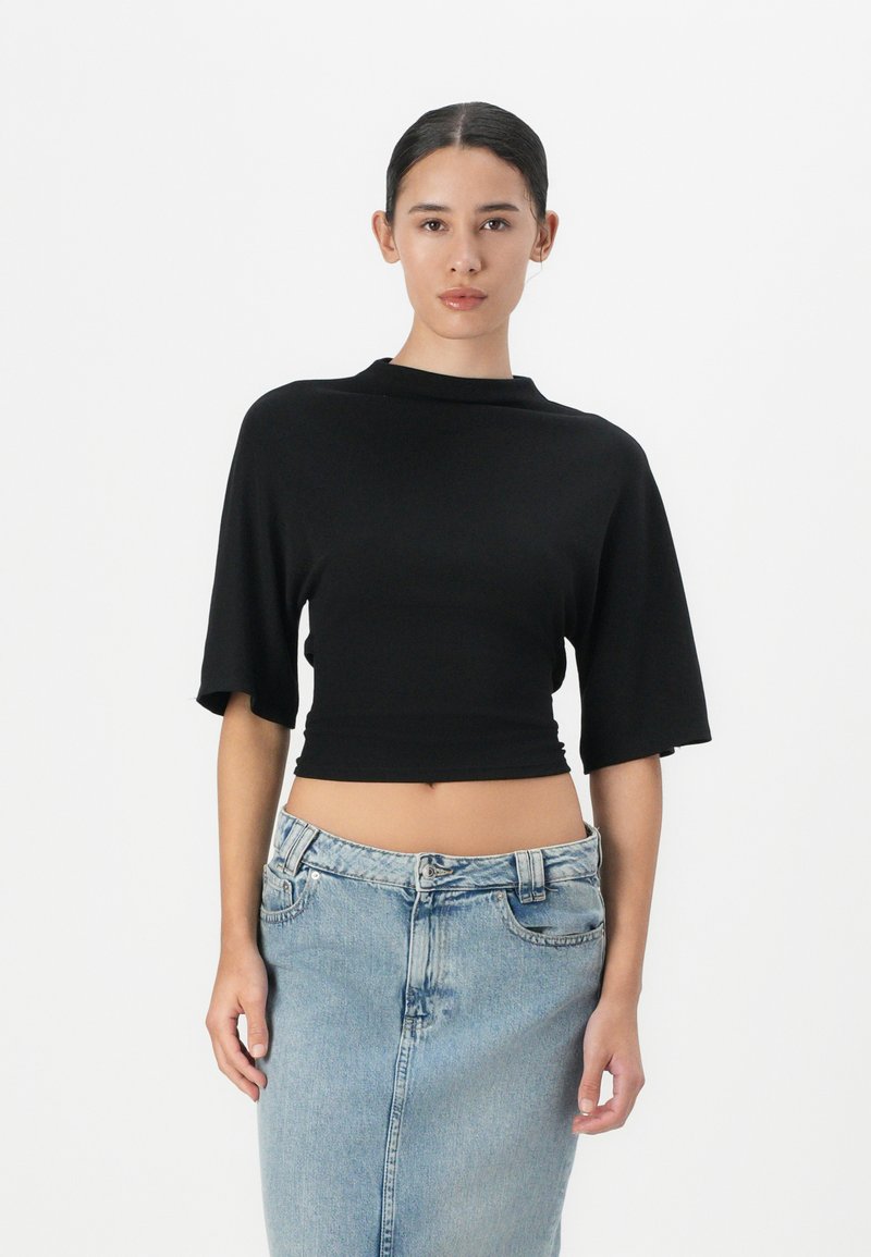 Zwarte cropped top met korte mouwen en een hoge halslijn. Gepaarde met een lichtblauwe denim rok met een split aan de voorkant en knoopsluiting.