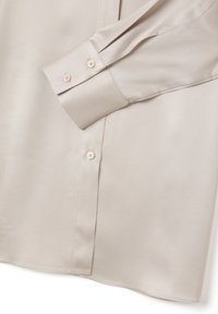 Beige Langarmhemd mit glatter Textur, Ein-Knopf-Manschetten und spitzem Kragen. Mit klaren Linien und minimaler Detailgestaltung.