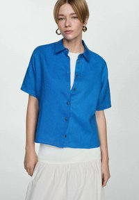 Camicia a maniche corte azzurra con bottoni in un tessuto leggero, caratterizzata da un colletto, chiusura frontale con bottoni e una vestibilità rilassata. Texture e colore distintivi.