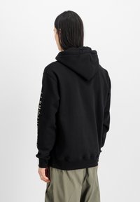 Sudadera con capucha negra de corte relajado, que presenta un logo en la manga izquierda, puños acanalados y una textura de tela suave.