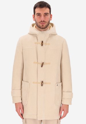 Uomo che indossa un cappotto toggole in corduroy beige con cappuccio, due grandi tasche frontali e cinturini alle maniche, in piedi contro uno sfondo semplice.