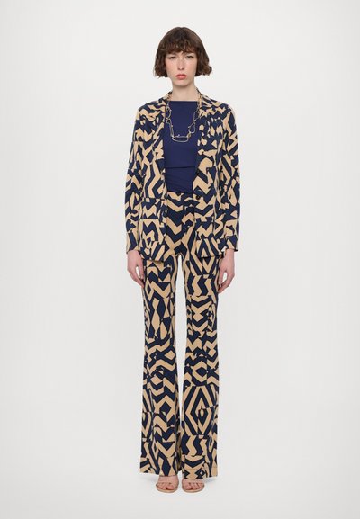 Navy and beige patterned blazer and wide-leg pants set, featuring geometric designs. Accompanied by a dark blue top and layered chain necklace.