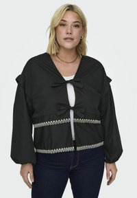 Czarna krótka kurtka z długimi rękawami, z dwoma kokardami z przodu i białą koronką na brzegu. Miękki materiał o luźnym kroju.