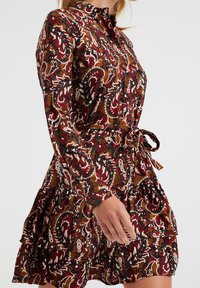 Abito a maniche lunghe con motivo floreale paisley, caratterizzato da ricchi colori bordeaux, verde e marrone, con orlo a balze e dettaglio con cintura in vita.