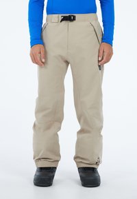 Beige skibroek met verstelbare tailleband, voorkruisen en elastische boorden. De gestructureerde stof biedt duurzaamheid; gecombineerd met zwarte laarzen.