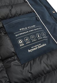 Interno di una giacca a vento nera con una tasca in tessuto blu navy, etichettata con dettagli sui materiali: poliestere riciclato, resistente al vento, traspirante, isolante e idrorepellente.