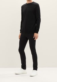 Suéter negro de manga larga con cuello redondo, hecho de una tela lisa. Combinado con jeans negros ajustados y zapatillas blancas.