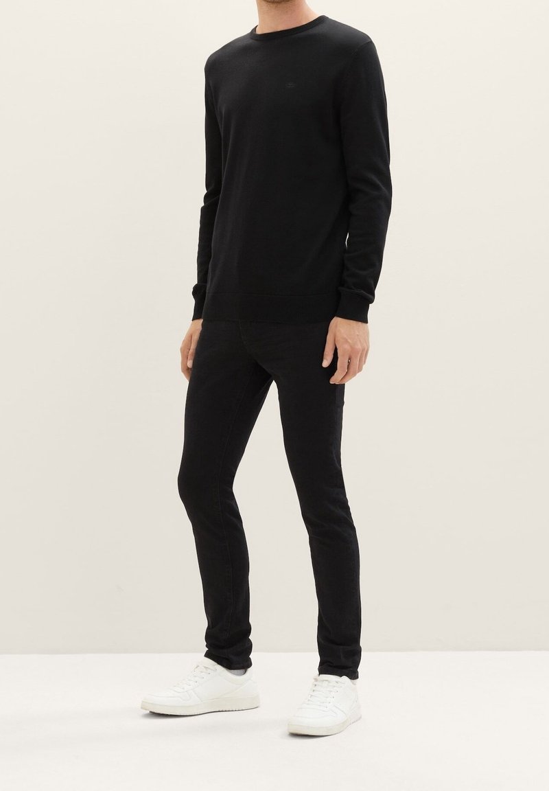 Suéter negro de manga larga con cuello redondo, hecho de una tela lisa. Combinado con jeans negros ajustados y zapatillas blancas.