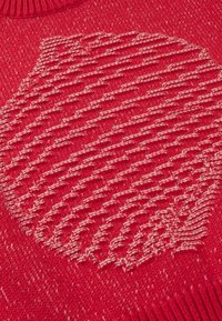 Tissu tricoté rouge avec un motif circulaire texturé blanc et rouge au centre et un bord de col côtelé en haut.